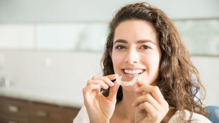 mujer sostiene en sus manos alineador dental invisible